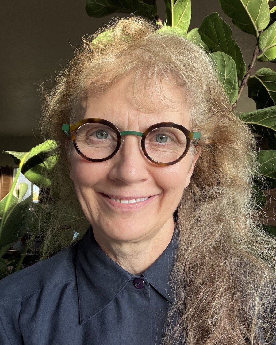 Dr. Shelley Perkins, smiling, wearing round tortoiseshell glasses and a blue shirt.